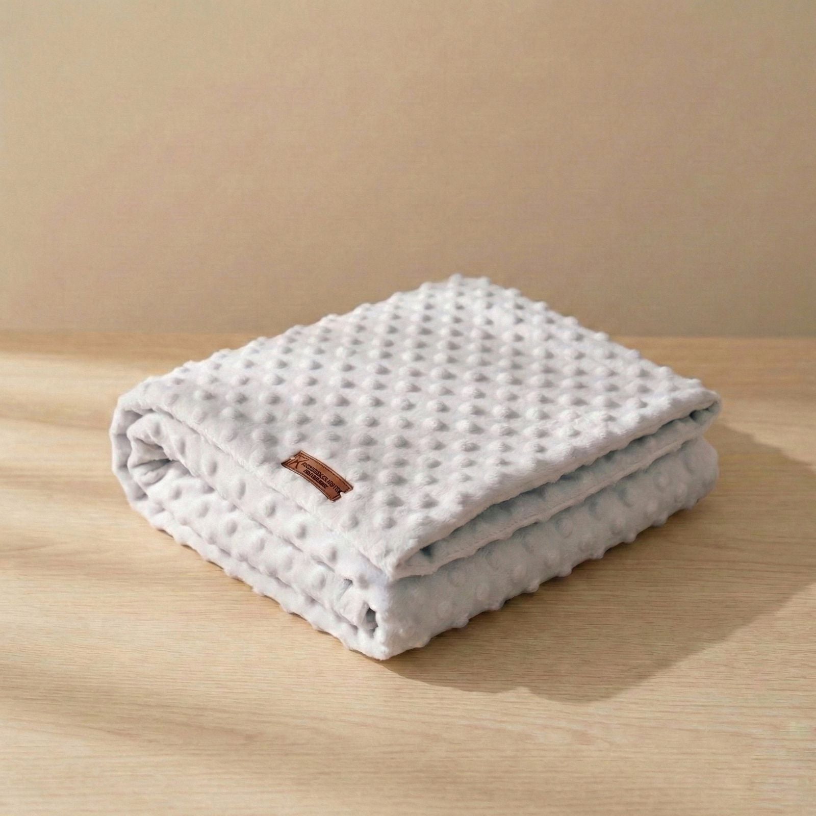 Manta minky gris perla para bebé doblada, con textura de puntos en relieve, sobre mesa de madera