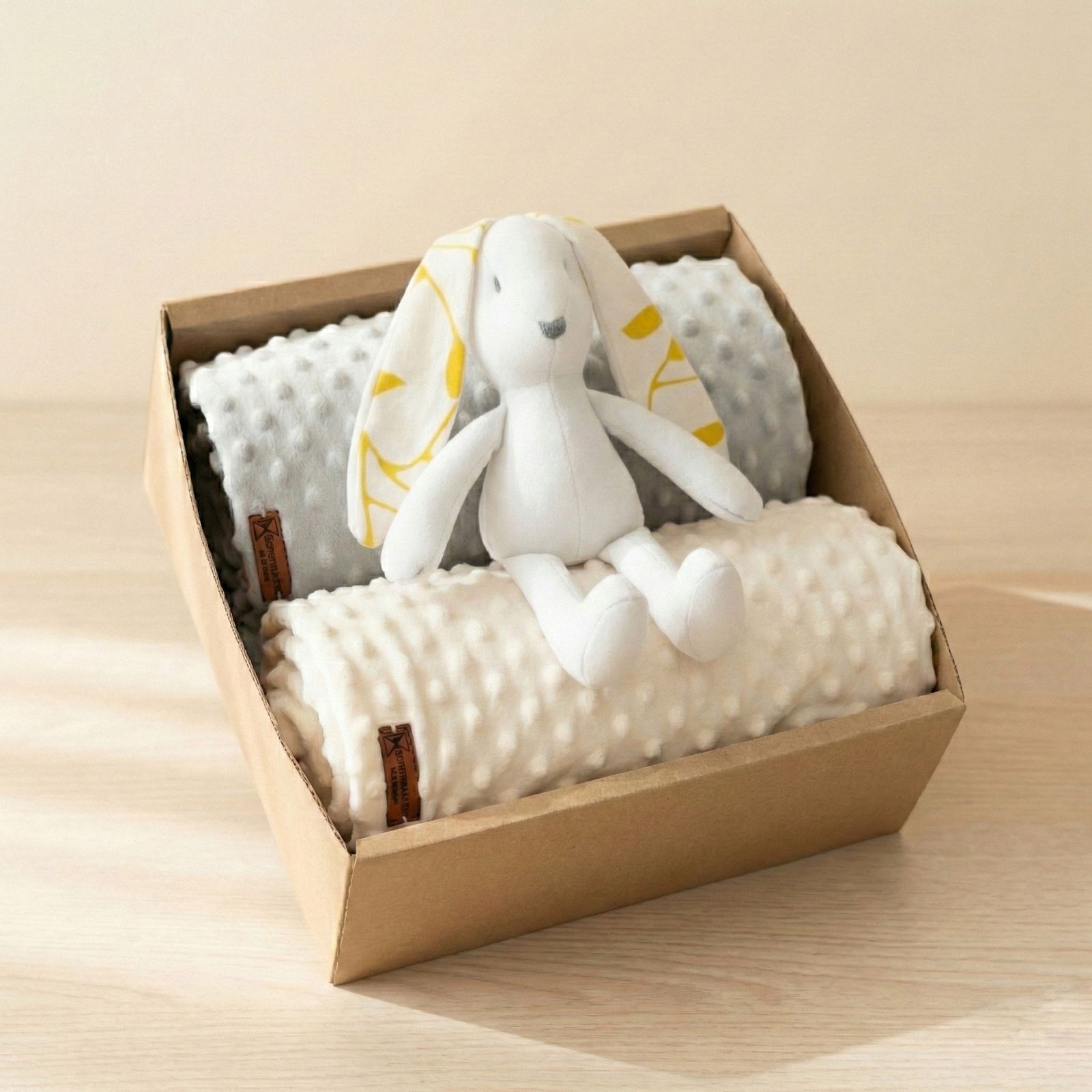 Caja regalo para bebé con dos mantas minky con textura de puntos en tonos neutros y peluche conejito blanco con orejas estampadas encima