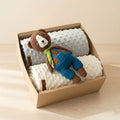Caja regalo para bebé con dos mantas minky con textura de puntos en tonos neutros y osito tejido a mano amigurumi con overol azul encima