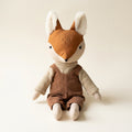 Zorrito de tela hecho a mano con overol de pana café y suéter beige, sobre fondo crema