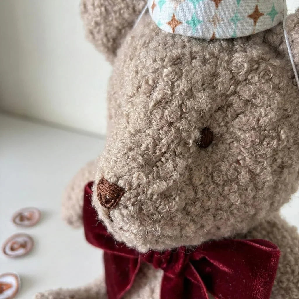 Detalle macro del pelo rizado bouclé, la nariz bordada y el gorro del osito de los meses